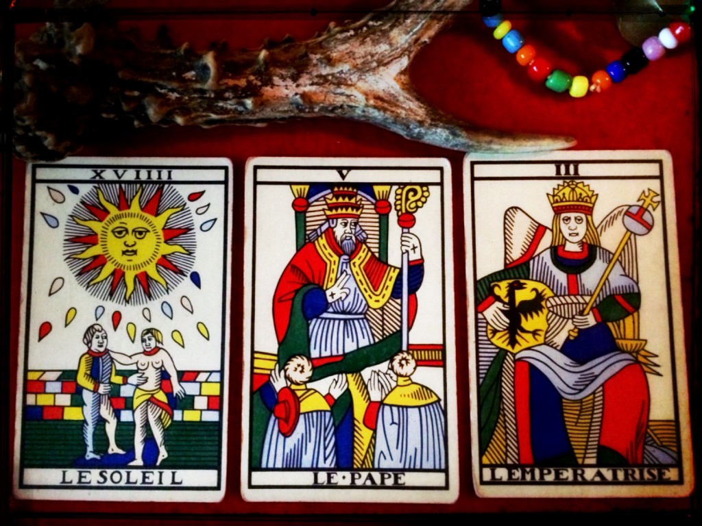 three tarot cards -- the sun, the pope, and the empress -- on a red table cloth