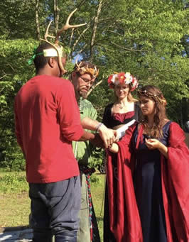 MayKing Jupiter and MayQueen Joy Leaf enacting the sacred marriage as our High Priest Phoenix wraps their hands in 5 strands of wool yarn our coven previously charged for the purpose of union. (Heron Michelle as High Priestess assists in the background.) Thus, the hand-fasting was made, merging the Lord and Lady, the anima and animus within each of us, uniting the land and her people, as they "tie the knot." The knot was then added as a talisman to the coven's besom. Photo used with permission.