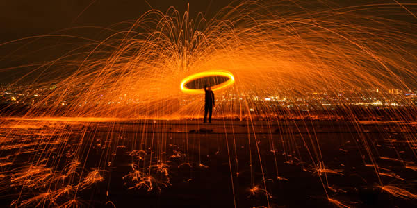 a man spinning a burning object creating a ring of fire and sparks shooting from it