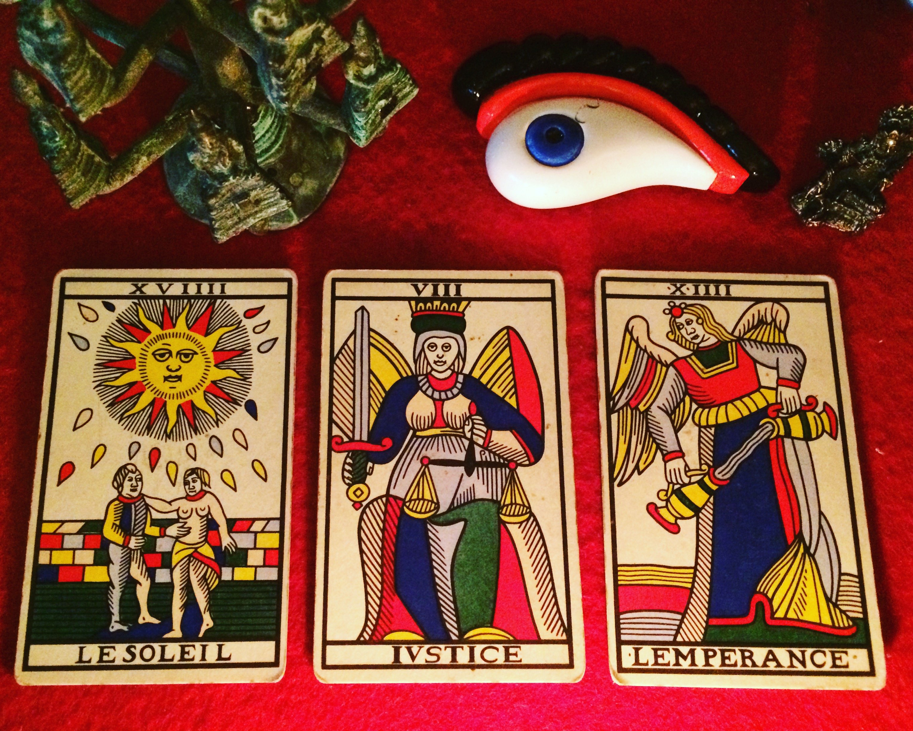 three tarot cards laid out on a red cloth: the sun, justice, and temperance