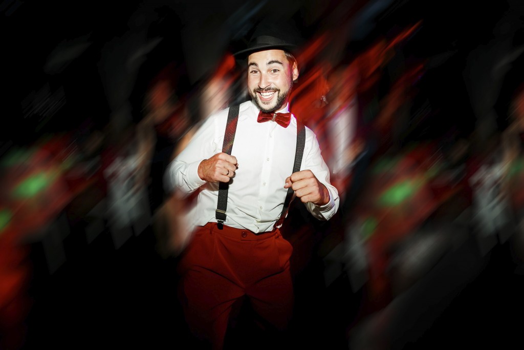 The groom dancing on dance floor, moving in motion. Cheerful man in hat, with mustache, beard and bow tie with suspenders. White shirt and red pants. Wedding color style Marsala. Having fun on party.