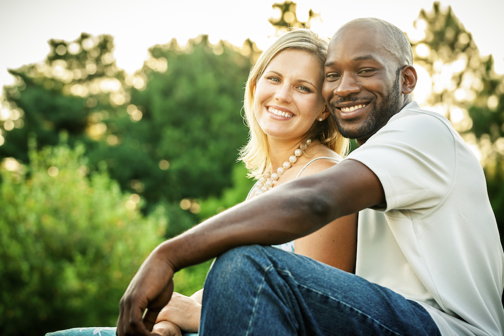 Beautiful mixed race couple or friends sitting at a park in the summer