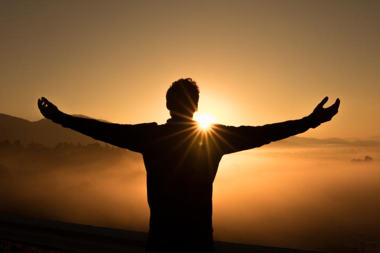 A man with outstretched arms in front of a sun rise