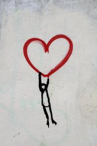 person hanging onto a heart by their finger tips.