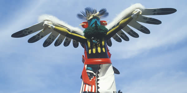 Hopi Kachina doll with outstretched winged arms against blue sky