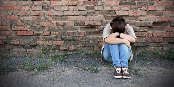 Young woman in despair sitting against a brick wall