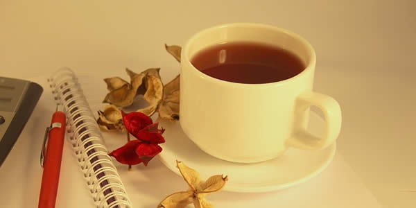 a cup of tea, a notebook, and a pen