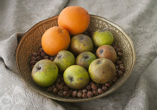 A bowl with oranges, apples, and chestnuts in it