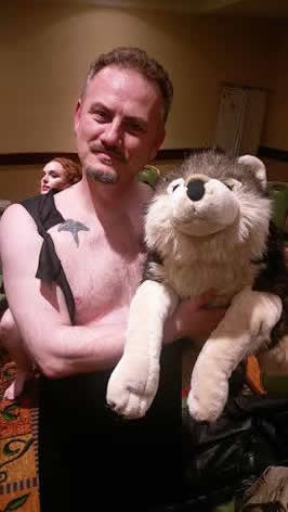 A man in a vest holding a stuffed doll of a wolf