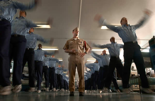 a drill instructor and a room full of cadets doing jumping jacks