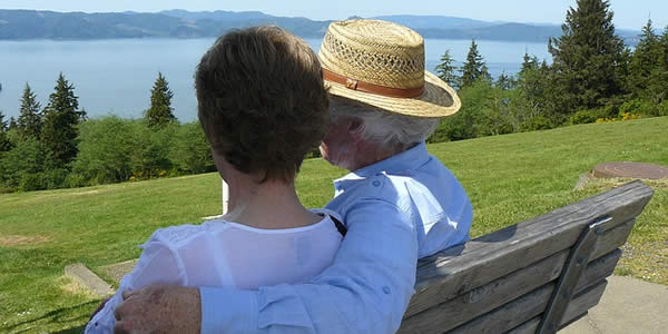 an elderly couple, a man and a woman, sit on a bench enjoying the outdoors