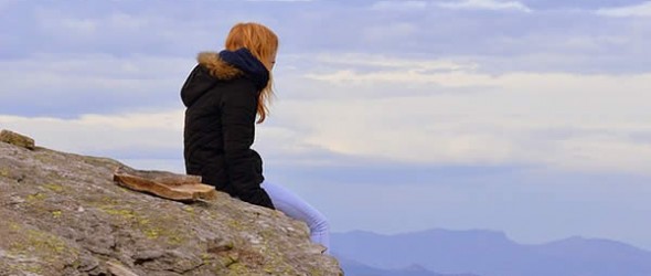 a woman sits on the edge of a cliff looking into the distance
