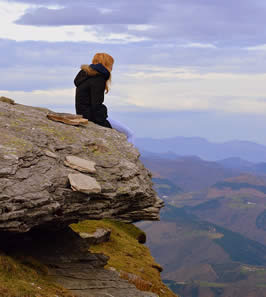 a woman sits on a cliff looking into the distance
