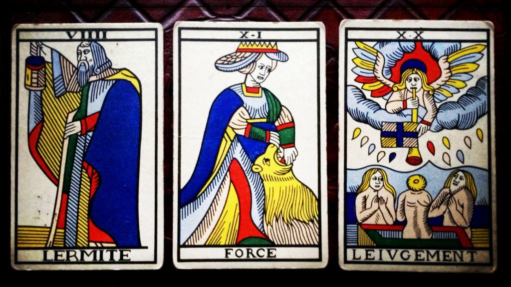 close up of three cards of the marseille tatot:  the hermit, strength, and judgement.