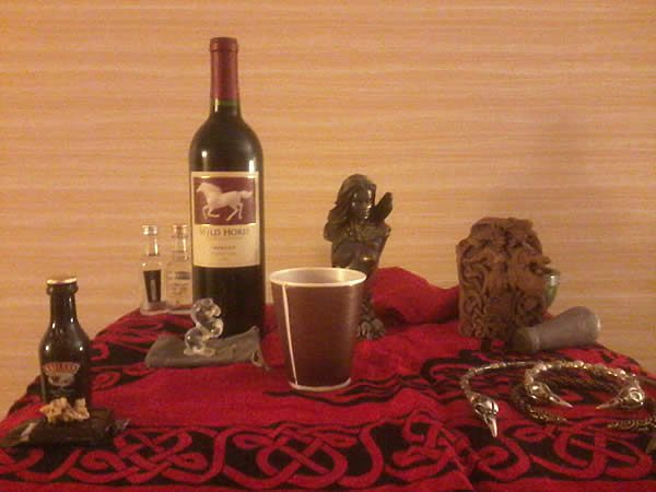 a small table covered with a red cloth with wine and other offerings placed on it