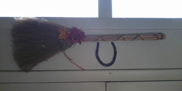 a handmade broom wrapped with ribbon hung above a horseshoe over a door