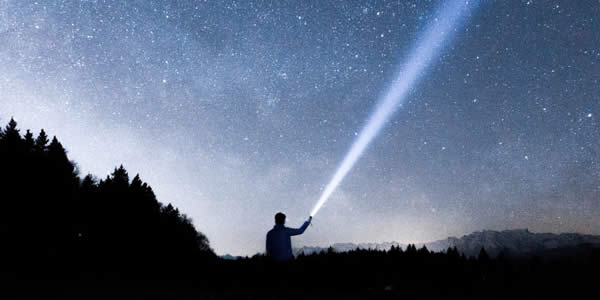 a man at night pointing a lit flashlight to the sky