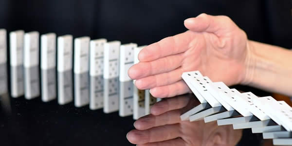 a hand blocking the fall of a line of dominoes