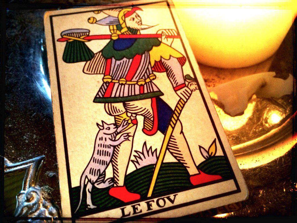 a tarot card, the fool, next to a lit candle on a table