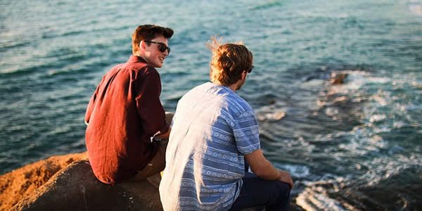 two men sitting next to a river conversing