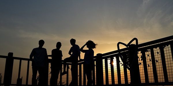 four frends leaning against a railing with the sun setting behind them
