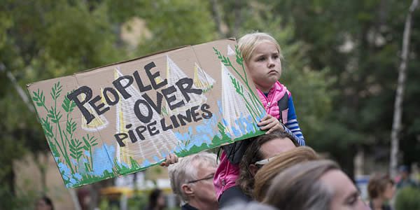 a young girl holds a sign reading "people over pipelines"