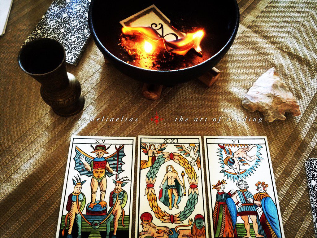 a photograph of three tarot cards placed near a calduron in which a fire burns