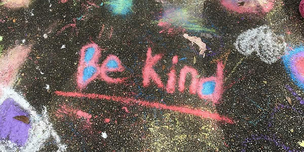 the words "be kind" written in colorful chalk on a sidewalk