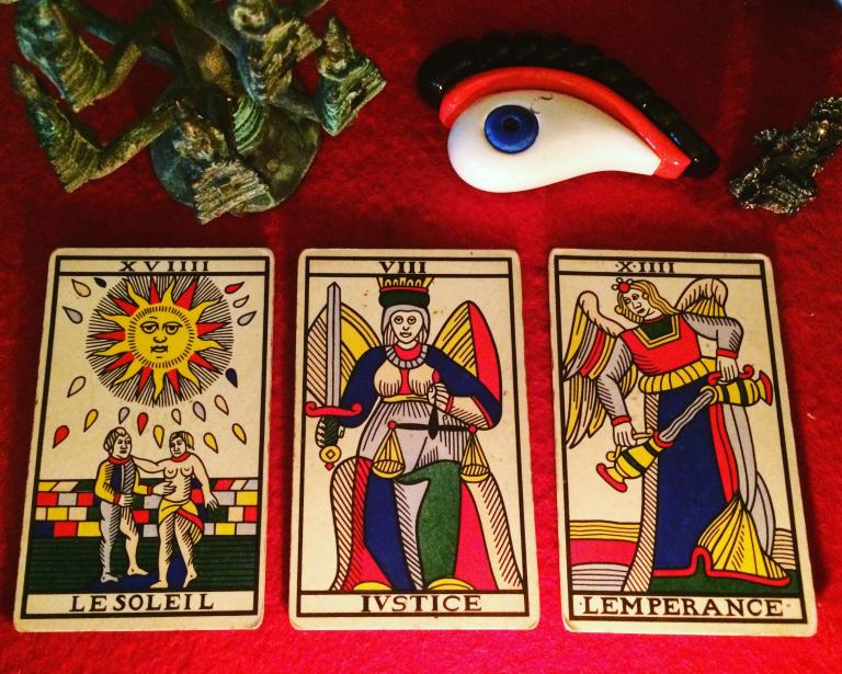 three tarot cards laid out on a red cloth:  the sun, justice, and temperance
