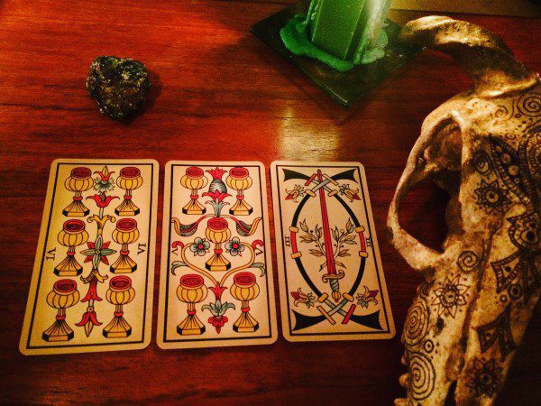 three cards placed on a table near a candle, a stone, and a decorative animal skull