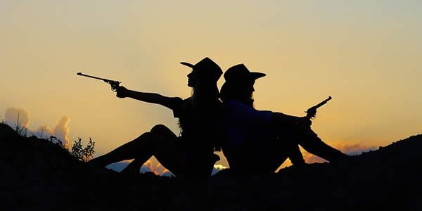 two women sillohuetted by the setting sun holding pistols