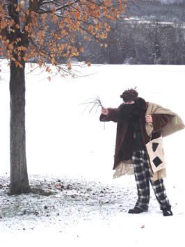 a man dressed in earth tones holding a switch and carrying a sack of toys