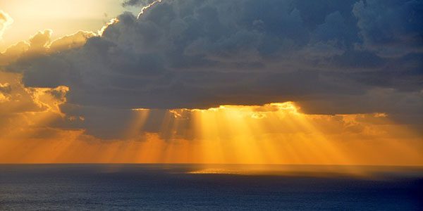 a sunset over the ocean with the sun hidden behind the clouds