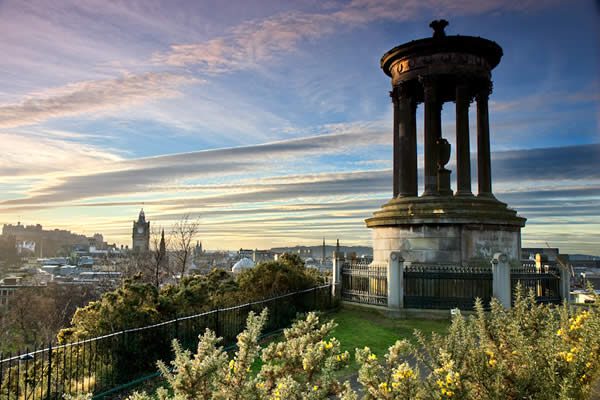 a photograph at sunset overlooking edinburg from a hill on which a moment stands