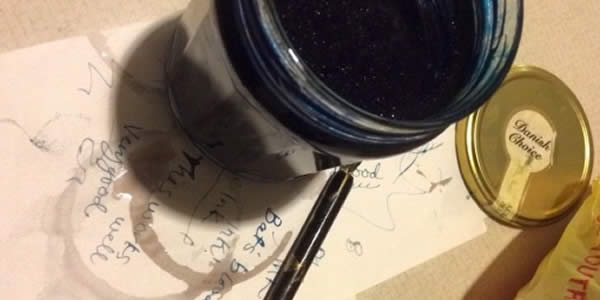 a jar of ink, a pen, and a piece of paper with scribbles on it