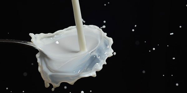 milk pouring into and overflowing a small glass on a field of black