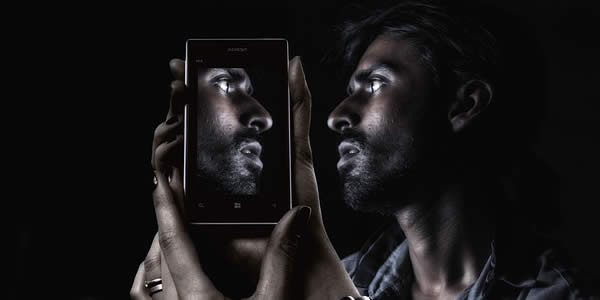 a man holds his cell phone reflecting his face