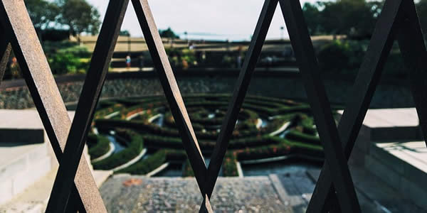 a hedge maze photographed during the day through an iron fence