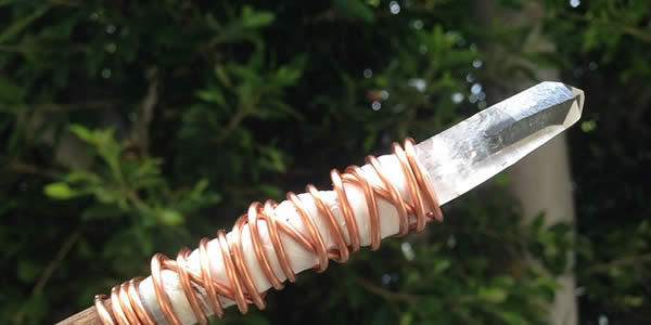 a wooden wand with a clear quartz point affixed with copper wire