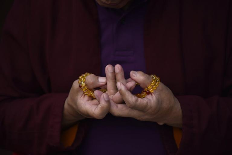 Hands of a buddhist monk offering prayer with beads