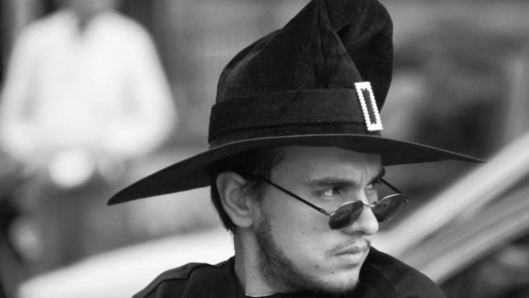 A masculine appearing witch in a pointy witch hat with hip sunglasses and facial hair