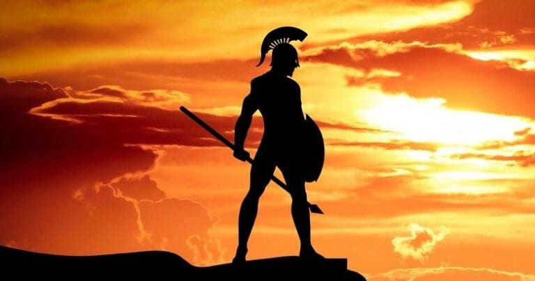 A cameo of a Spartan warrior holding a spear and shield is standing on a cliff face with an orange sky background.
