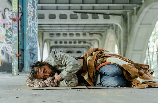 Homeless man asleep on mat, covered with blanket