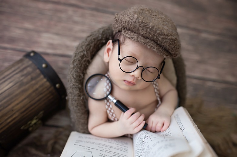 Baby with glasses, hat, book, magnifying glass. Baby Sherlock Holmes