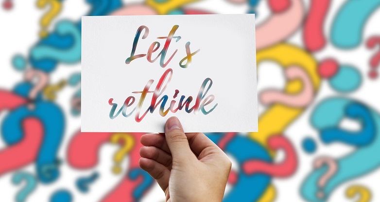"Let's rethink" written in colorful lettering, held in hand.. Colorful question marks in background.