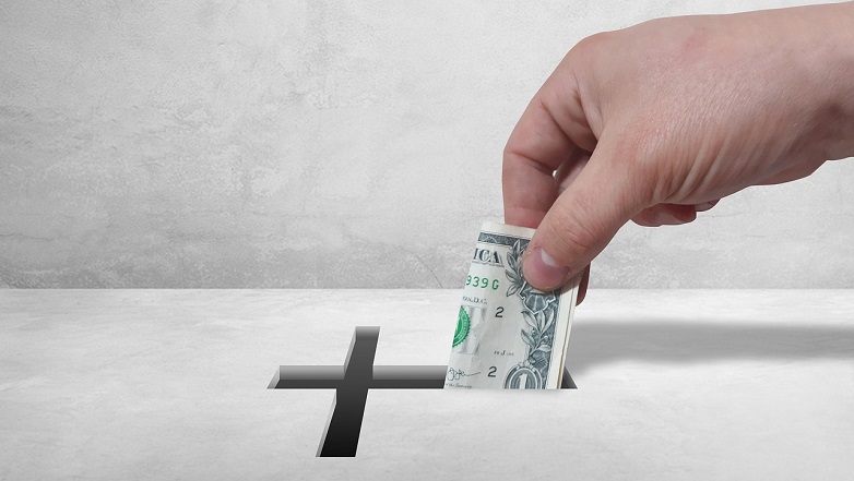 Pastors (and Others) Exempt from Tithing. Hand putting dollar into cross-shaped hole in box