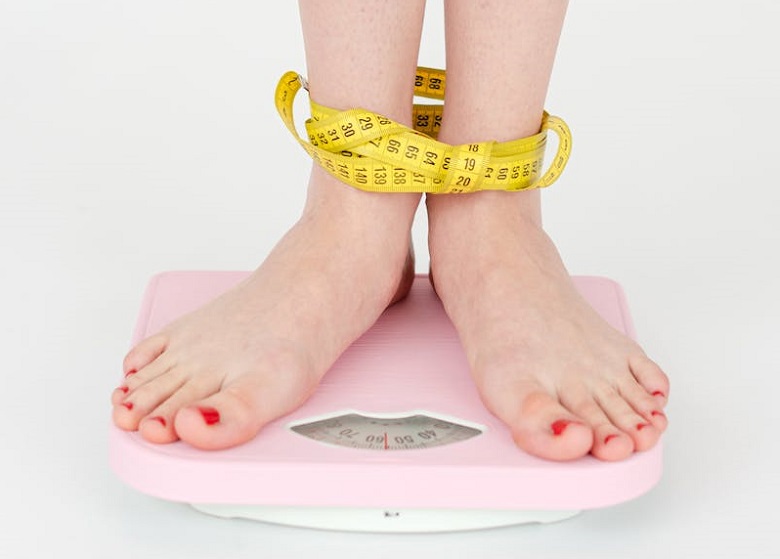 Female feet standing on scale, bound by measuring tape