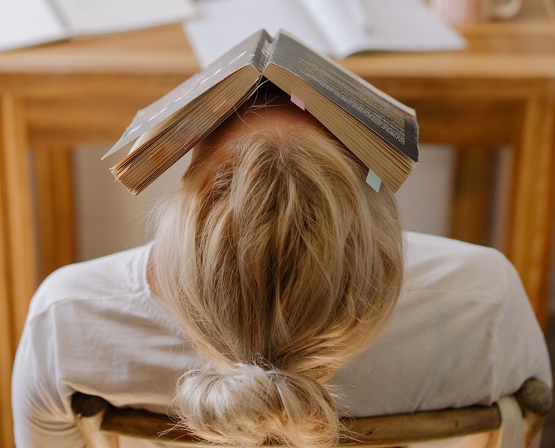 Blonde person in white shirt with book on face