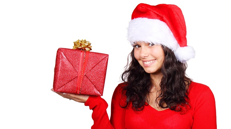 Woman in red shirt and Santa hat holding red Christmas gift