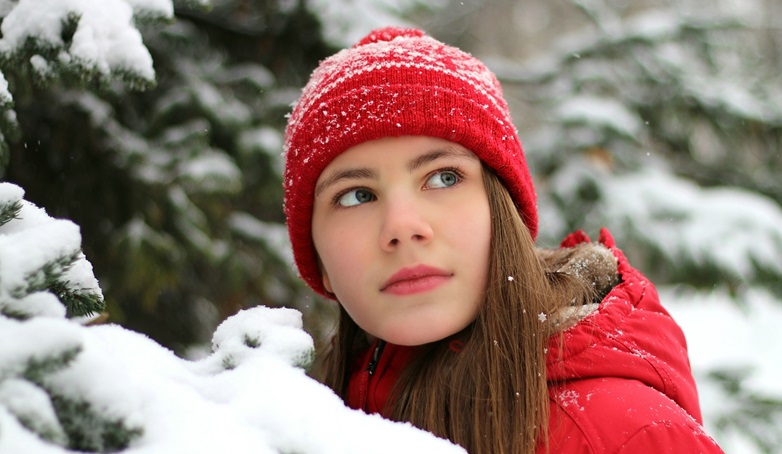 Woman with red coat and hat, in front of green pine tree with snow